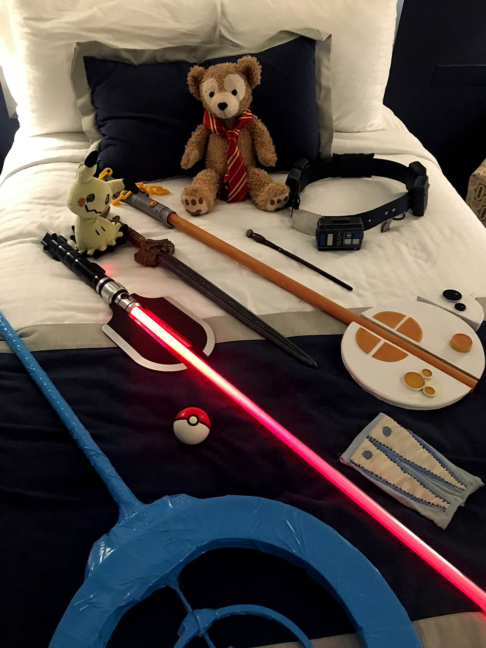 A Pokestop, lightsaber, keyblade, sword and Duffy on the bed.