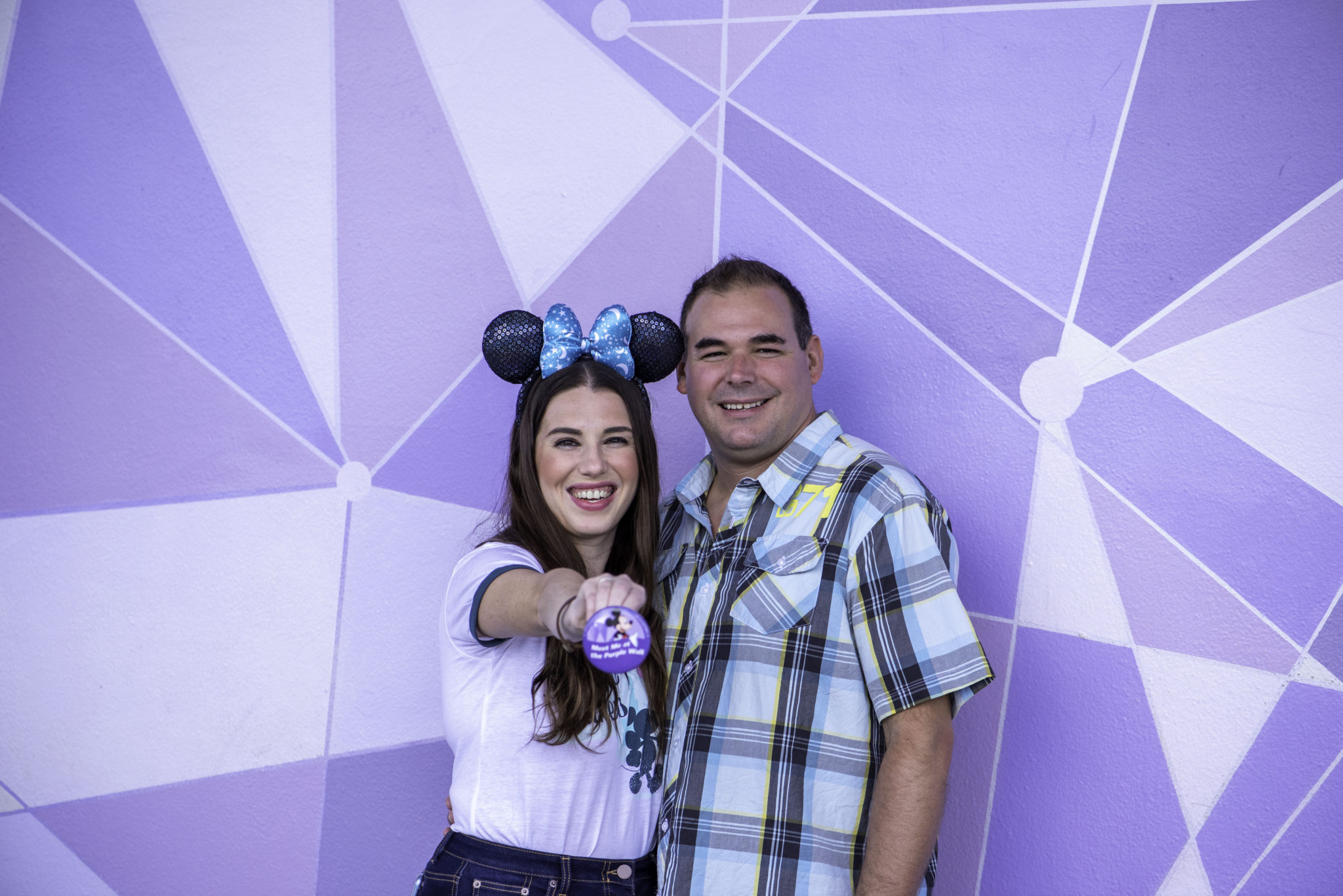 Chelsea and Jay holding the meet me at the Purple Wall Button in front of the new Purple Disney Walls